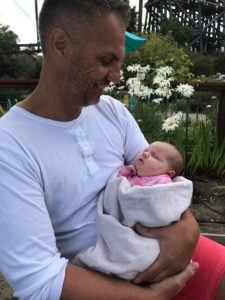 A father and client of Circle Surrogacy holds his baby while sitting in the garden.